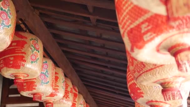 Linternas de papel en un edificio de mala calidad. Faroles de papel rojo colgando en el techo del edificio del templo de hormigón envejecido en el día soleado en el país oriental. decoración tradicional — Vídeo de stock