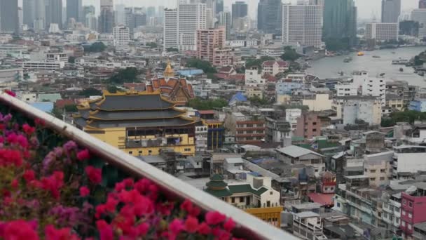 Vista dos edifícios tradicionais e modernos da cidade oriental. Belo canteiro de flores contra a paisagem urbana de casas tradicionais e arranha-céus no dia nebuloso em ruas de Bangkok ou Krungtep . — Vídeo de Stock