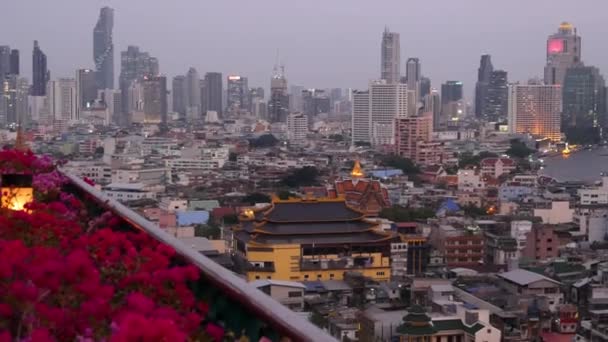 Pohled na tradiční a moderní budovy orientálního města. Krásné květinové záhony proti městskému prostředí tradičních domů a mrakodrapů v zamlžený den v ulicích Bangkoku nebo Krungtepu. — Stock video