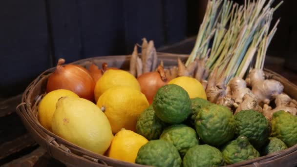 Korg med frukt och grönsaker. Flätad korg med olika citrusar och grönsaker placerade på golvet nära trävägg — Stockvideo