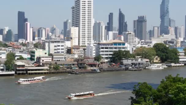 Dzielnica finansowa w pobliżu spokojnej rzeki. Widok drapaczy chmur położonych na brzegu spokojnej rzeki Chao Praya w centrum Bangkoku. Panorama wielkiego miasta. Łodzie na wodzie w Krungthep. — Wideo stockowe