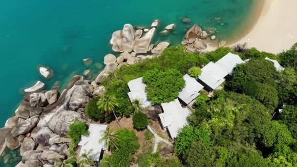 Små hus på tropisk ö. Små mysiga bungalows ligger på stranden av Koh Samui Island nära lugnt hav på solig dag i Thailand. Vulkaniska stenar och klippor drönare ovanifrån. — Stockvideo