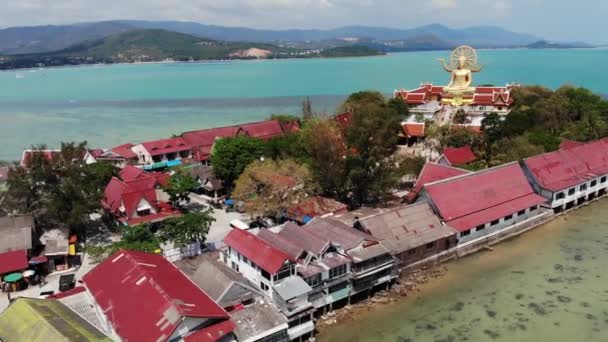 Ilha com templo budista e muitas casas. Vista aérea da ilha com templo budista com estátua Grande Buda cercado por casas tradicionais em palafitas na baía do oceano Pacífico em Samui, Tailândia. — Vídeo de Stock