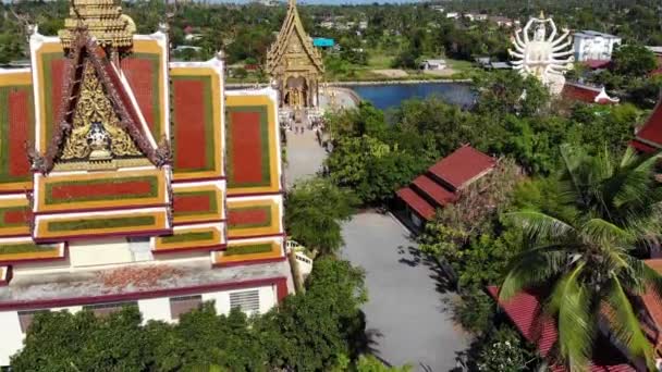 Βουδιστικός ναός κοντά στη λίμνη. Κηφήνας top θέα από στέγες και αγάλματα του υπέροχο βουδιστικού ναού που βρίσκεται κοντά στη λίμνη την ηλιόλουστη μέρα στο Κο Σαμούι. Wat Plai Λαέμ με χαμογελαστή Βούδα και Guan Yin — Αρχείο Βίντεο