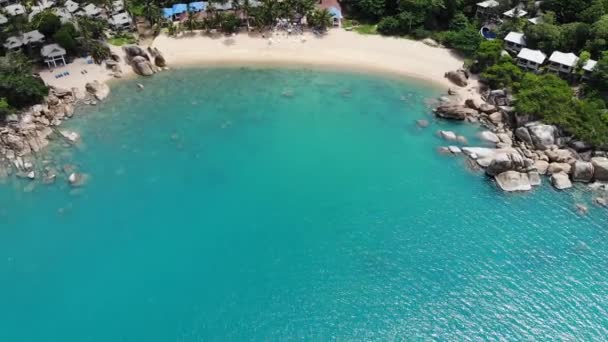 Små hus på tropisk ö. Små mysiga bungalows ligger på stranden av Koh Samui Island nära lugnt hav på solig dag i Thailand. Vulkaniska stenar och klippor drönare ovanifrån. — Stockvideo