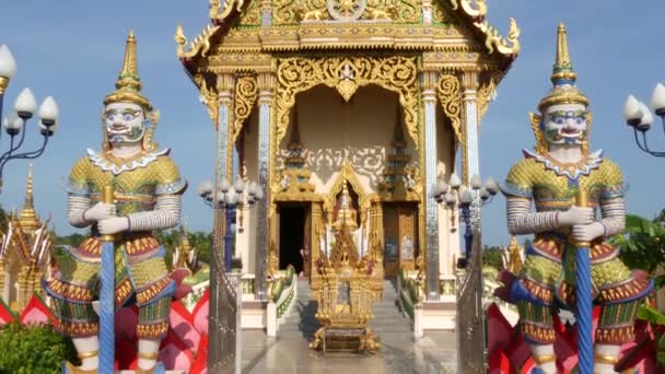 Kleurrijke standbeelden in de buurt van de Aziatische tempel. Twee heldere veelkleurige standbeelden gelegen in de buurt van de decoratieve boeddhistische tempel op zonnige dag in Oosterse land. Mythische reus Guardian yak in wat Plai Laem. Koh Samui. — Stockvideo