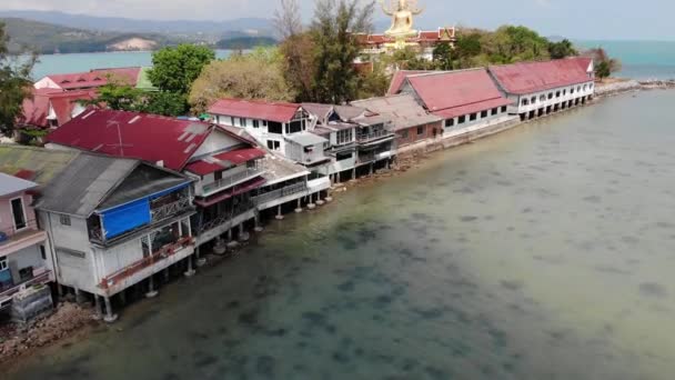 Isola con tempio buddista e molte case. Veduta aerea dell'isola con tempio buddista con statua Big Buddha circondato da case tradizionali su palafitte nella baia dell'oceano Pacifico a Samui, Thailandia. — Video Stock