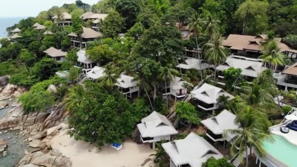 Kis házak a trópusi szigeten. Apró hangulatos bungalók található partján Koh Samui sziget közelében nyugodt tenger napsütéses napon Thaiföldön. Vulkáni sziklák és sziklák drón tetejére néző. — Stock videók