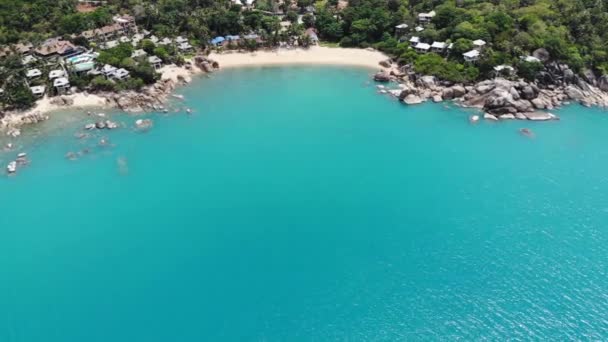 Małe domki na tropikalnej wyspie. Małe przytulne bungalowy położone na brzegu wyspy Koh Samui w pobliżu spokojnego morza w słoneczny dzień w Tajlandii. Wulkaniczne skały i klify drona widok z góry. — Wideo stockowe