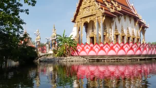 Barevné sochy poblíž asijského chrámu. Dvě zářivě barevné sochy umístěné nedaleko ozdobného buddhistického chrámu v slunečném dni v orientální krajině. Mystický strážný v Wat Plai Laem. Koh Samui. — Stock video