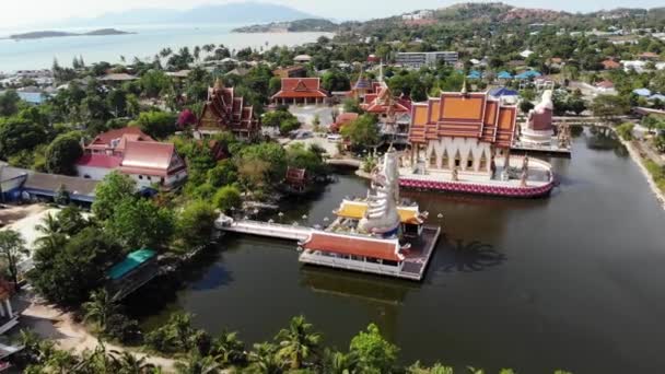 Buddhistiskt tempel nära sjön. Drone topputsikt över tak och statyer av underbara buddhistiska tempel ligger nära sjön på soliga dagen på Ko Samui. Wat Plai Laem med leende Buddha och Guan Yin — Stockvideo