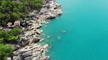 Tropikal adada küçük evler. Güneşli Tayland 'da güneşli bir günde, Koh Samui adasının kıyısındaki küçük, rahat bungalovlar. Volkanik kayalar ve uçurumlar insansız hava aracı görüntüsü.