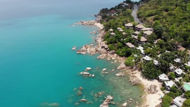 Små hus på tropisk ö. Små mysiga bungalows ligger på stranden av Koh Samui Island nära lugnt hav på solig dag i Thailand. Vulkaniska stenar och klippor drönare ovanifrån. — Stockvideo