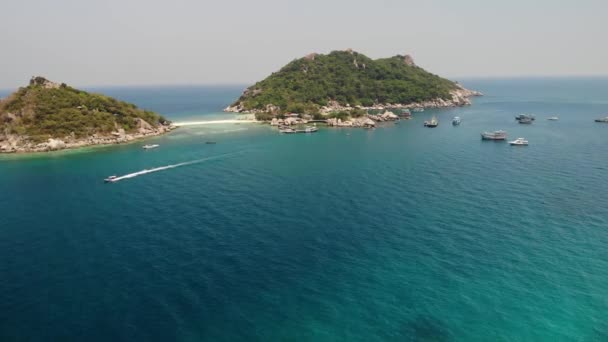 小さな島の近くのボートや桟橋。タイの晴れた日にビーチや桟橋に接続されたユニークな小さな島の近くの穏やかな青い海に浮かぶモーターダイブボート。ナン元コタオ. — ストック動画