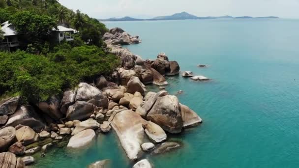 Small houses on tropical island. Tiny cozy bungalows located on shore of Koh Samui Island near calm sea on sunny day in Thailand. Volcanic rocks and cliffs drone top view. — Stock Video