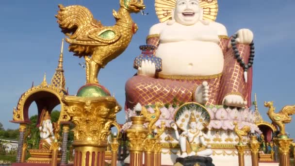 Hotei standbeeld buiten boeddhistische tempel. Traditionele Happy Hotei sculptuur gelegen in erf van het boeddhisme heiligdom tegen wolkenloze blauwe hemel in Aziatische land. Wat Plai Laem. Koh Samui. — Stockvideo