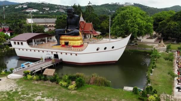 池の船上の黒僧の像。タイのサムイ島の小さな池に船の形をした構造の真ん中に位置する巨大な黒い僧侶の彫刻。ドローンビュー. — ストック動画