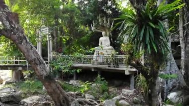 Koh Samui Adası 'ndaki Hin Lad Ulusal Parkı' nın yeşil ormanındaki geleneksel tapınağın yakınındaki nehrin yanındaki Beyaz Buda heykeli. Mercek parlıyor, güneş ışınları yeşilin içinden geçiyor.