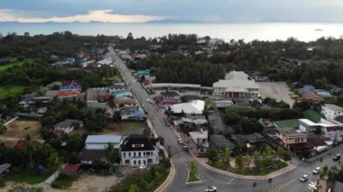 Arabalar ormanın yakınındaki küçük bir kasabada döner kavşakta ilerliyorlar. Küçük bir kasabanın ortasında, Koh Samui Adası Tayland 'daki denize karşı dairesel kavşakta giden araçlar. Drone görünümü