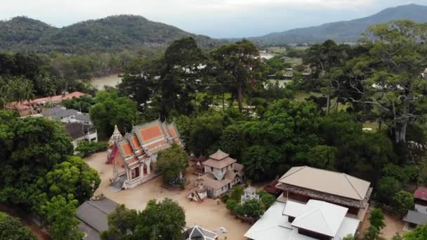 Κλασικός βουδιστικός ναός ανάμεσα στο δάσος. Από πάνω δείτε drone κλασικό βουδιστικό μοναστήρι μεταξύ πράσινα δέντρα κοντά στο λόφο στην Ταϊλάνδη. Κο Σαμούι. έννοια του τουρισμού, διαλογισμό και ανατολίτικη ζωή — Αρχείο Βίντεο