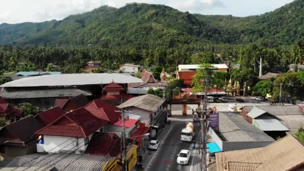 Voitures circulant le long de la route près des portes du temple. Véhicules circulant le long de la route asphaltée à travers une petite ville près des portes du temple oriental traditionnel dans le district de Lamai sur l'île de Koh Samui en Thaïlande. Vue sur drone . — Video