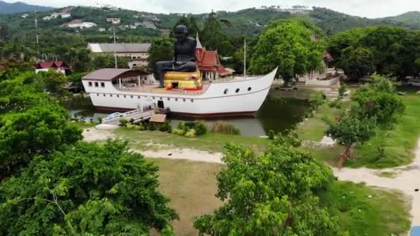 Gölette gemide siyah keşiş heykeli. Tayland Koh Samui Adası'nda küçük bir gölet gemi şeklinde yapının ortasında bulunan büyük siyah keşiş heykel. Drone görünümü. — Stok video