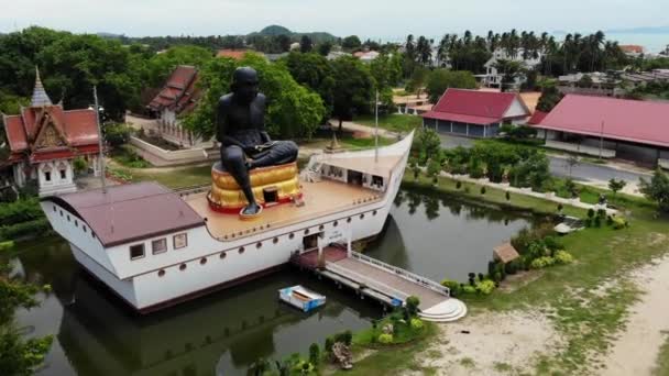 Zwarte monnik standbeeld op schip in vijver. Enorme zwarte monnik sculptuur gelegen in het midden van het schip gevormde structuur in kleine vijver op Koh Samui eiland in Thailand. Drone-weergave. — Stockvideo