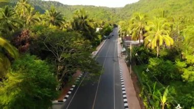 Yerleşim ve orman boyunca asfalt yol. Asfalt yolu Koh Samui Cennet Adası 'ndaki küçük tipik yerleşim yerlerinden ve yeşil tropikal yağmur ormanlarından geçiyor. Ufuktaki dağlar. Köy hayatı