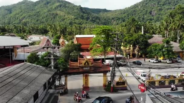 Auto's rijden langs de weg in de buurt van Temple Gates. Voertuigen rijden langs asfalt weg door kleine stad in de buurt van poorten van de traditionele Oosterse tempel in Lamai district op het eiland Koh Samui in Thailand. Drone-weergave. — Stockvideo