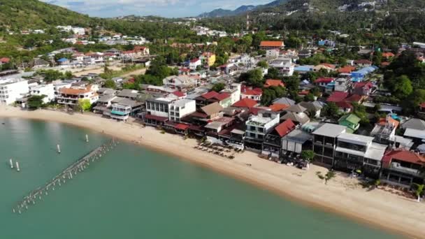 Fisherman village on seashore. Aerial view of typical touristic place on Ko Samui island with souvenir shops and walking street on sunny day. Architecture in asia, local settlement drone view — Stock Video