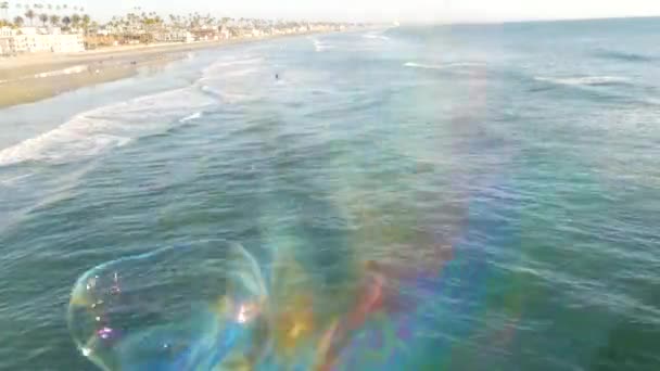 Zeepbellen blazen op de oceaanpier in Californië, wazig zomertijd achtergrond. Creatieve romantische metafoor, concept van droomgeluk en magie. Abstract symbool van kindertijd, fantasie, vrijheid — Stockvideo