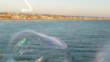 Kaliforniya 'da okyanus rıhtımında sabun köpüğü üflemek, yaz arkaplanını bulanıklaştırmak. Yaratıcı romantik metafor, hayal kurmak mutluluk ve sihir. Çocukluğun soyut sembolü, fantezi, özgürlük