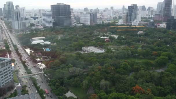 大都市の緑の公園。道路近くのルンピニ公園の緑の木のドローンビューとバンコク、タイの通りに高層ビル — ストック動画