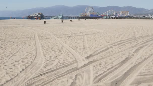 Óceánhullámok és homokos kaliforniai strand, klasszikus óriáskerék a vidámparkban a Santa Monica-i mólón, csendes óceáni üdülőhely. Nyári ikonikus kilátás, Los Angeles szimbóluma, CA USA. Utazási koncepció — Stock videók