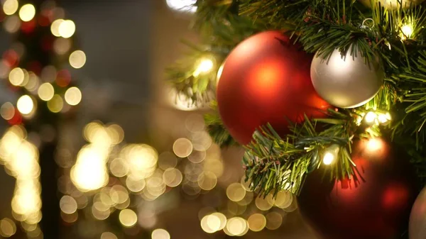 Closeup of Festively Decorated Outdoor Christmas tree with bright red balls on blurred sparkling fairy background. Defocused garland lights, Bokeh effect. Merry Christmas and Happy Holidays concept