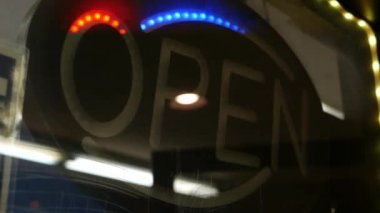 Karanlıkta parlayan açık neon ışığı. Cam pencerenin girişinde canlı retro stil metin var. Renkli elektrikli pankart seçici odaklanma. Ampuller gece parlıyor. Parlak parlak harfler.