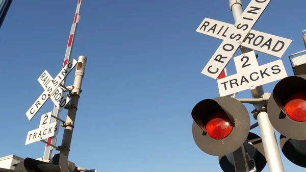 Level crossing warning signal in USA. Crossbuck notice and red traffic light on rail road intersection in California. Railway transportation safety symbol. Caution sign about hazard and train track.