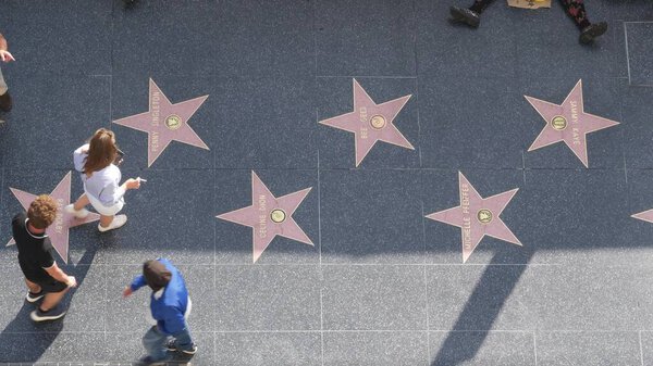 LOS ANGELES, CALIFORNIA, USA - 7 NOV 2019: Walk of fame promenade on Hollywood boulevard in LA. Pedastrians walking near celebrity stars on asphalt. Walkway floor near Dolby and TCL Chinese Theatre.
