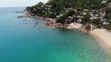 Tropikal adada küçük evler. Güneşli Tayland 'da güneşli bir günde, Koh Samui adasının kıyısındaki küçük, rahat bungalovlar. Volkanik kayalar ve uçurumlar insansız hava aracı görüntüsü