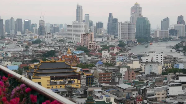 View of traditional and modern buildings of oriental city. Beautiful flowerbed against cityscape of traditional houses and skyscrapers on misty day on streets of Bangkok or Krungtep