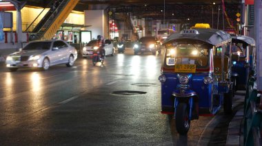 BANGKOK, THAILAND - 18 ARALIK 2018: Geleneksel Tayland taksisi - Tuk Tuk yol boyunca turistleri bekliyor. Kalabalık şehrin gece trafiği. Asya ülkesinin sembolü, eşsiz bir araç..