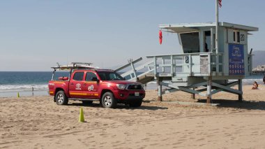 Santa Monica, LOS ANGELES CA ABD - 28 OCT 2019 Kaliforniya yaz plaj estetiği. İkonik mavi ahşap gözetleme kulesi, kumlu sahilde kırmızı cankurtaran arabası. Eğlence parkı ve rıhtımdaki eğlence.
