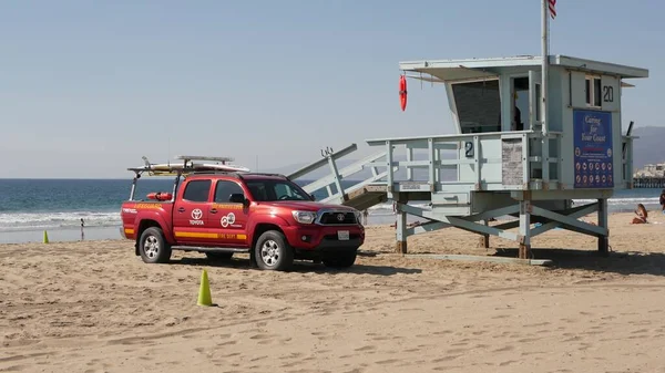 Santa Monica, LOS ANGELES CA ABD - 28 OCT 2019 Kaliforniya yaz plaj estetiği. İkonik mavi ahşap gözetleme kulesi, kumlu sahilde kırmızı cankurtaran arabası. Eğlence parkı ve rıhtımdaki eğlence.