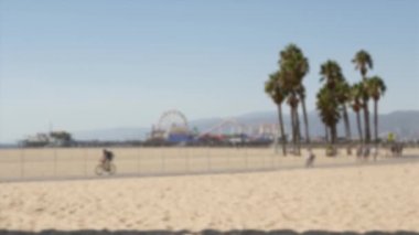 Kaliforniya plaj estetiği, insanlar bisiklet yolunda bisiklet sürüyor. Bulanık, odaklanmış arka plan. Santa Monica Amerikan Pasifik Okyanusu Tatil Köyü, Los Angeles CA ABD 'deki iskele ve palmiyelerdeki eğlence parkı.