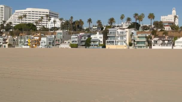 Kaliforniya yazları plaj estetiği, güneşli mavi gökyüzü, kum ve deniz kenarındaki birçok farklı hafta sonu evi. Deniz kenarındaki binalar, Santa Monica Pasifik Okyanusu kıyısındaki emlak merkezi, Los Angeles CA USA — Stok video