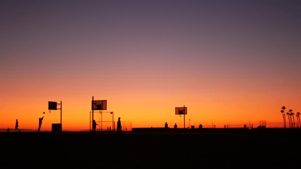 Californie été crépuscule plage esthétique, coucher de soleil rose. Silhouettes méconnaissables, les gens jouent avec la balle sur le terrain de basket-ball. Station balnéaire de Newport près de Los Angeles CA USA. Gradient de ciel violet — Video