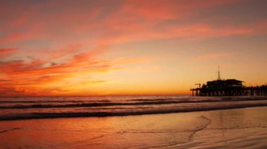 Kaliforniya yazları plaj estetiği, altın gün batımı. Pasifik okyanusu dalgaları üzerinde canlı dramatik bulutlar. Santa Monica popüler tatil köyü, Los Angeles CA USA. Los Angeles 'ta atmosferik karamsar, mor bir akşam güneşi.