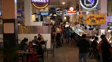 LOS ANGELES, CALIFORNIA, USA - 27 OCT 2019: Grand central market street lunch shops with diversity of glowing retro neon signs. Multiracial people on foodcourt. Citizens dining with fast food in LA. clipart