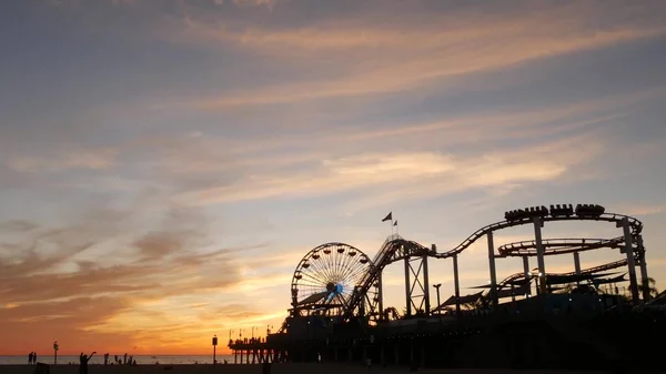 Classic ferris wheel, amusement park on pier in Santa Monica pacific ocean beach resort. Summertime California aesthetic, iconic view, symbol of Los Angeles, CA USA. Sunset golden sky and attractions.