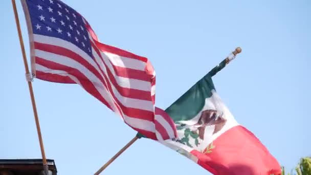 Üç renkli Meksika bayrağı ve rüzgarda dalgalanan Amerikan bayrağı. Meksika ve ABD 'nin iki ulusal simgesi gökyüzü, San Diego, California, ABD' ye karşı. Sınır, ilişki ve birlikteliğin siyasi sembolü — Stok video